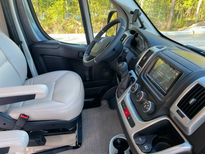Step inside this RV rental! View of a modern camper van cockpit with beige seats, steering wheel, and tech-filled dashboard.. Thor Scope 18M 2022