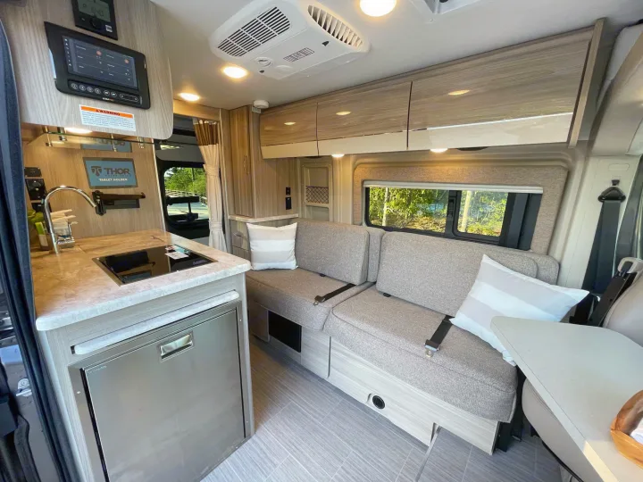 Modern RV rental interior with compact kitchen, sofa seating, and overhead cabinets for storage.. Thor Scope 18M 2022