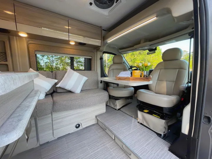 Inside a comfortable RV rental: modern living space with sofa, adjustable table, and swiveling front seats.. Thor Scope 18M 2022