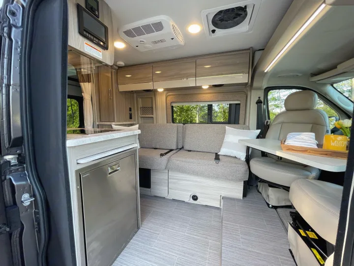 Modern RV rental interior: kitchen, flexible seating with table, swiveling front seats, and ample storage in a camper van.. Thor Scope 18M 2022