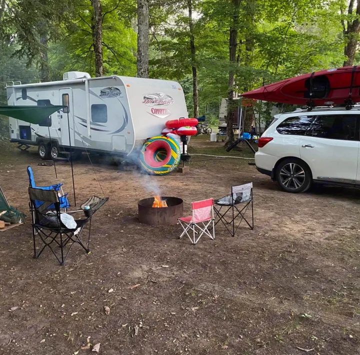 Enjoying the outdoors with an RV rental! A cozy campsite scene with a travel trailer, SUV with kayak, and a glowing campfire.. Jayco Coyote 2014