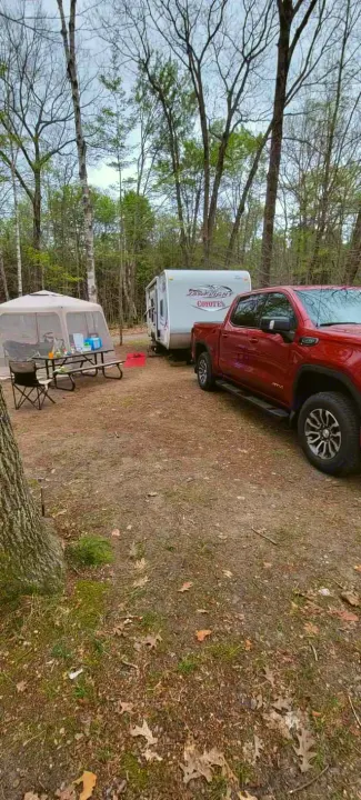 A red pickup truck & travel trailer (rv rental) parked at a wooded campsite with a screened tent, picnic table, and chairs.. Jayco Coyote 2014
