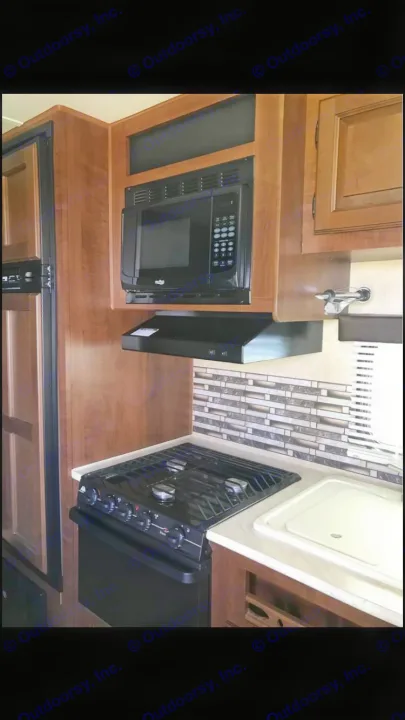 View of a well-equipped RV rental kitchen, showing microwave, stove, sink, and wood cabinetry with a tiled backsplash.. Jayco Coyote 2014