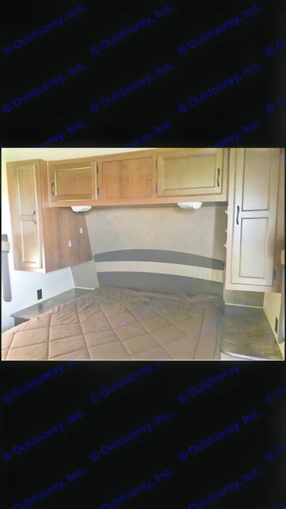 Cozy and compact RV rental bedroom featuring a brown bed, patterned headboard, and wood overhead cabinets.. Jayco Coyote 2014