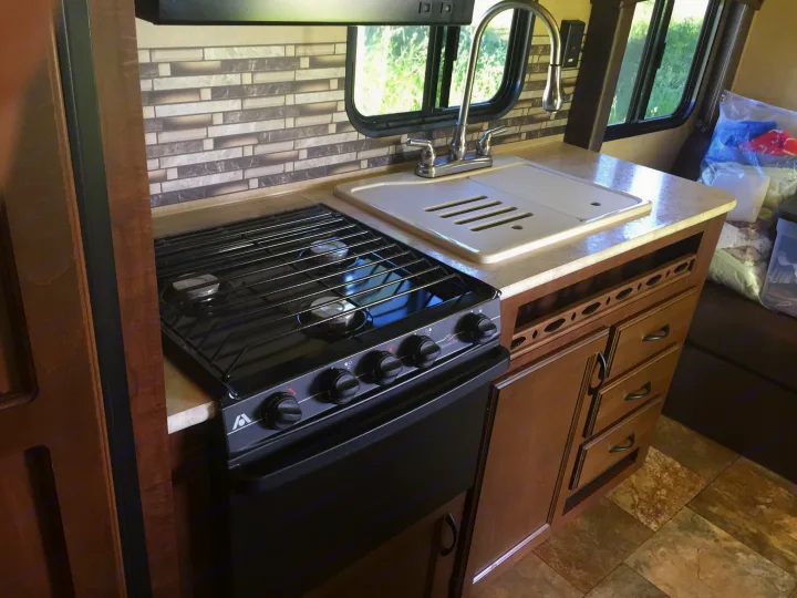 RV rental kitchen features a black gas stove, sink, and tiled backsplash, set against light countertops and wood cabinetry.. Jayco Coyote 2014
