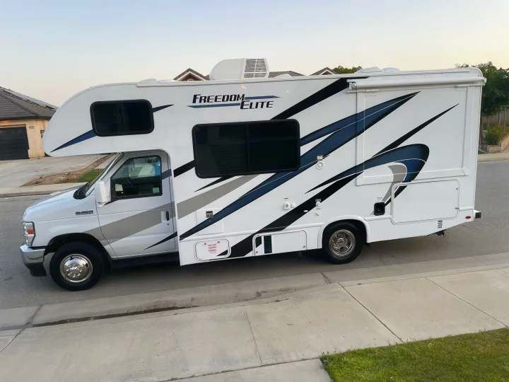 White Freedom Elite RV rental parked on a street, featuring sleek graphics and an awning. Perfect for your next adventure!. THOR MOTOR COACH FREEDOM ELITE 22fef 2022