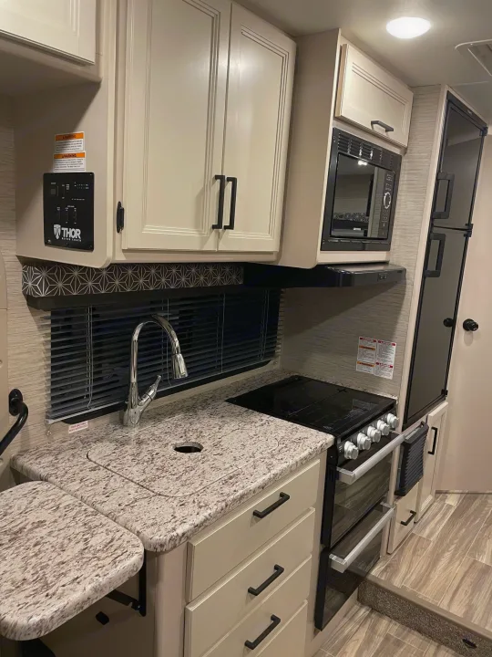 Compact yet functional RV rental kitchen: modern stove, microwave, large sink, ample counter space, cream cabinets, and full-size fridge.. THOR MOTOR COACH FREEDOM ELITE 22fef 2022