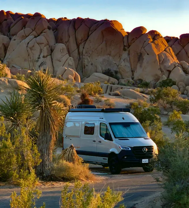 RV rental parked among Joshua Trees and desert rock formations at golden hour, ideal for national park adventures.. Winnebago Revel 2022
