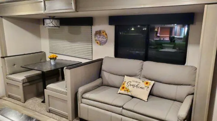 Spacious RV rental interior featuring a comfy sofa, a well-lit dining booth, and overhead storage.. Forest River PRIME TIME 2022
