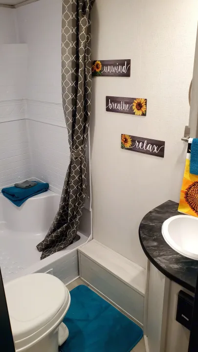 Cozy RV rental bathroom featuring a tub, shower, toilet, sink, and tranquil sunflower decor.. Forest River PRIME TIME 2022