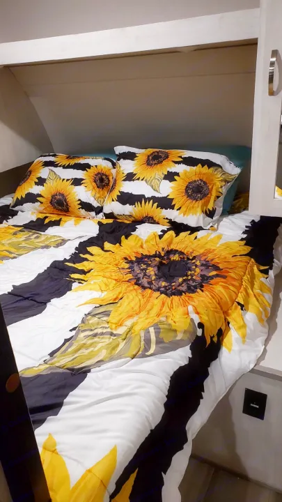 Cozy RV rental bed featuring a bright sunflower print comforter and pillows on black/white stripes.. Forest River PRIME TIME 2022
