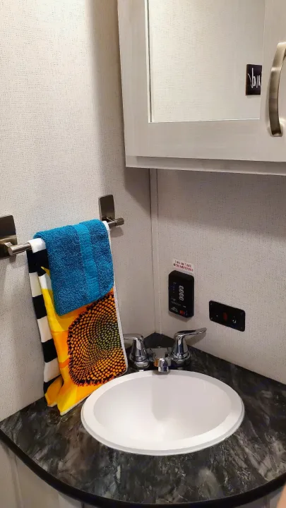 RV rental compact bathroom shows a sink, dark counter, chrome faucet, colorful towels, and a 'winterized' label.. Forest River PRIME TIME 2022