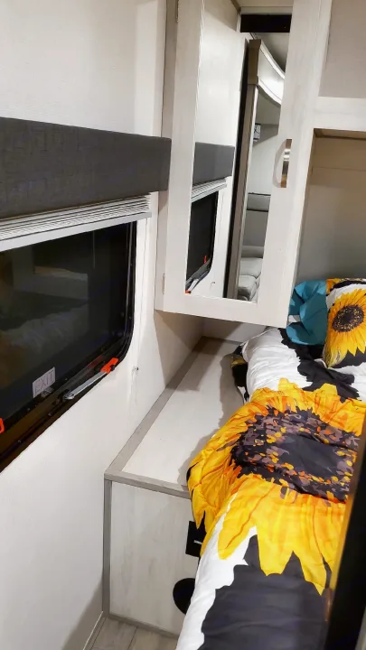 Cozy RV rental bedroom featuring a sunflower-patterned comforter, window with an exit sign, and mirrored cabinet.. Forest River PRIME TIME 2022