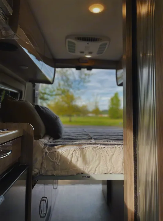 Interior of a modern RV rental, featuring a comfortable bed looking out to a grassy field. Ideal for travel.. Thor Sequence 2021