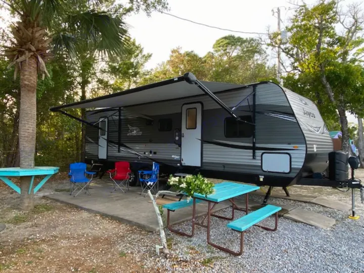 RV rental set up at a peaceful campsite with an extended awning, chairs, and a turquoise picnic table for outdoor leisure.. Jayco Jay Flight 2021