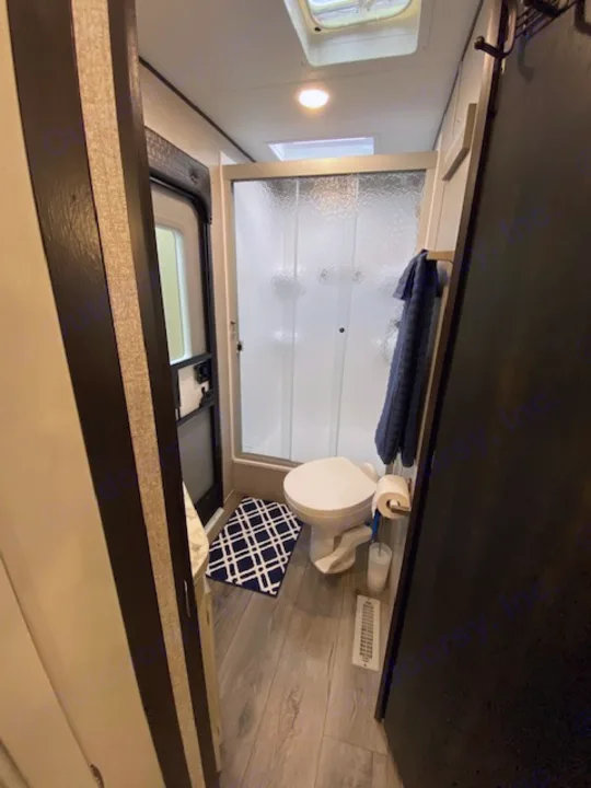 RV rental's compact bathroom features a shower, toilet, and a blue patterned mat on wood-look flooring.. Jayco Jay Flight 2021