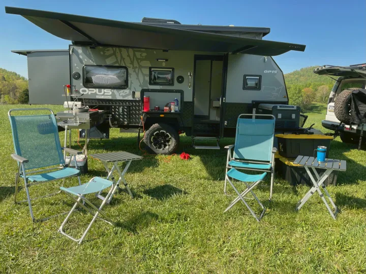 This off-road Opus OP15 rv rental is fully set up for camping, featuring an outdoor kitchen and chairs amidst nature.. Other Other 2022