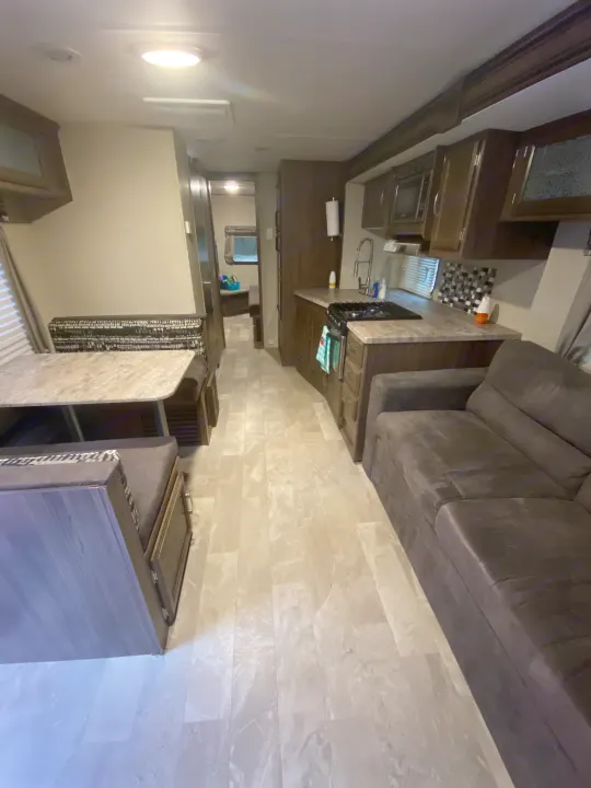 Modern RV rental interior: kitchen with dark cabinets & checkered backsplash, grey sectional sofa, light flooring.. Coachmen Other 2019