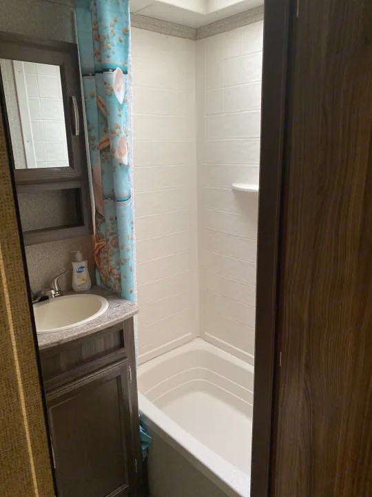 An RV rental bathroom featuring a sink, vanity with mirror, and a shower/bathtub. A blue seashell shower curtain is visible.. Coachmen Other 2019