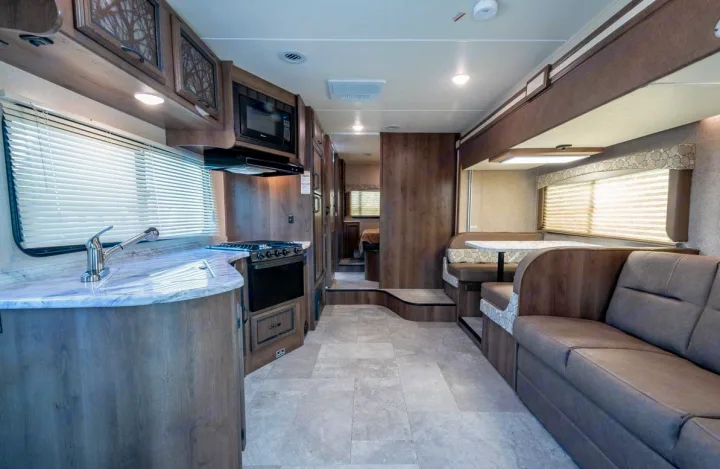 A bright RV interior showing a modern kitchen, dinette, and sofa, leading to a bedroom hallway. Perfect for an RV rental.. Coachmen Freelander 28BH 2018