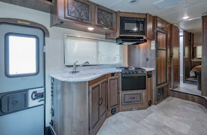 Modern RV rental kitchen with stove, microwave, fridge, sink, and ample counter space. Light-toned interior for travel comfort.. Coachmen Freelander 28BH 2018