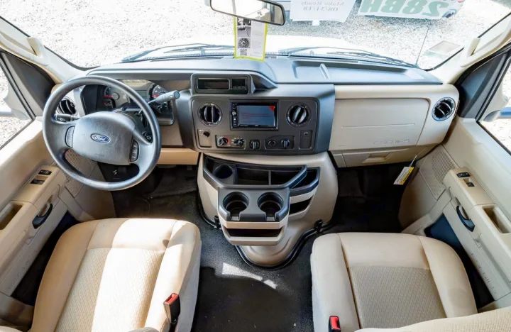 Spacious front cabin of an RV rental showing the Ford E-Series dashboard, steering wheel, and two light-colored seats.. Coachmen Freelander 28BH 2018