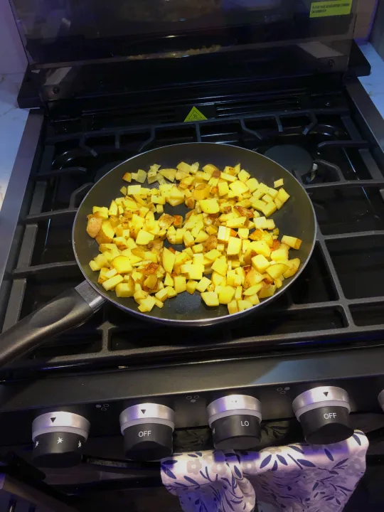 Golden diced potatoes sizzle in a pan on a modern stovetop, a cozy kitchen scene for an RV rental.. Forest River Cherokee Alpha Wolf 2022
