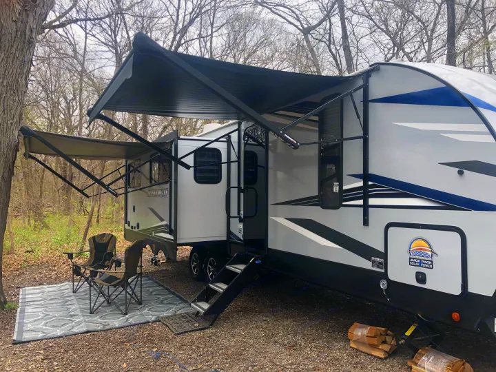 Spacious RV rental set up at a peaceful campsite with extended awnings, chairs, and mat, ready for outdoor relaxation.. Forest River Cherokee Alpha Wolf 2022