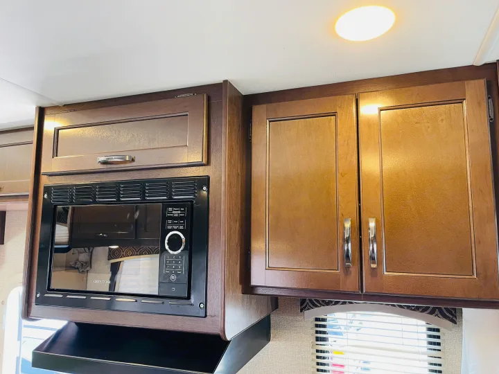 View of an RV rental's kitchen, showing a built-in microwave under warm wooden overhead cabinets.. Thor Chateau 2017