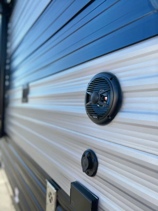 RV rental exterior: a "DRIVEN" outdoor speaker, utility port, & electrical outlet on striped siding.. Forest River Cherokee Wolf Pup 2022