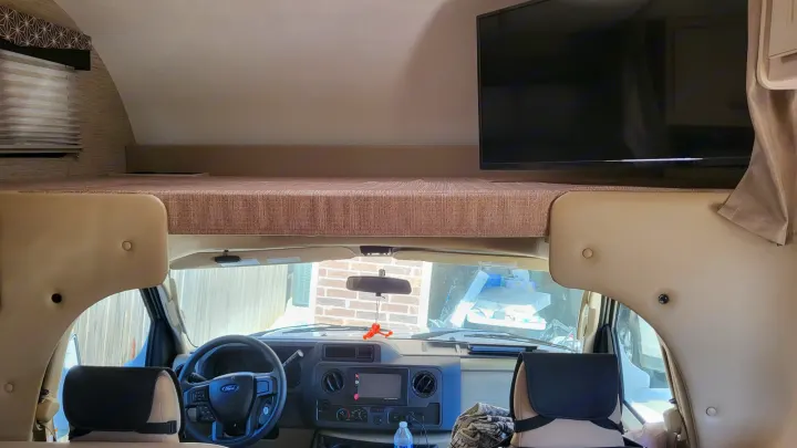 Inside an RV rental: view of the cab-over bunk, mounted TV, and driver's cockpit for your next motorhome adventure.. Ford Freedom Elite 2022