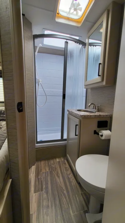 Compact RV rental bathroom features a curved shower, sink vanity, and toilet, optimizing space.. Ford Freedom Elite 2022