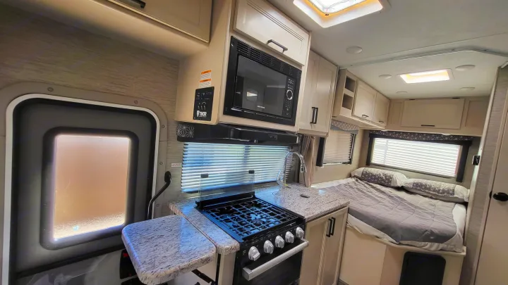 RV rental interior featuring a kitchenette with stove, microwave, and sink, alongside a cozy bedroom and main entry.. Ford Freedom Elite 2022