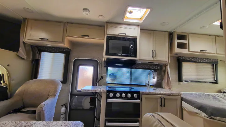 This RV rental's interior features a compact kitchen with a stove, microwave, and sink, a bed, and seating. Ideal for travel.. Ford Freedom Elite 2022