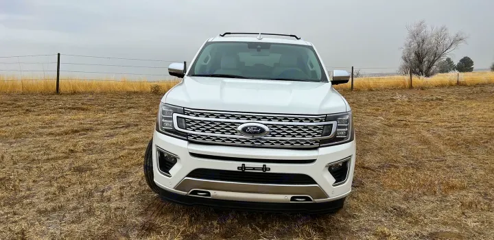 A white Ford Expedition SUV sits in a dry field under a cloudy sky. A spacious vehicle for trips, like an RV rental adventure.. Ford Ford Expedition 2021