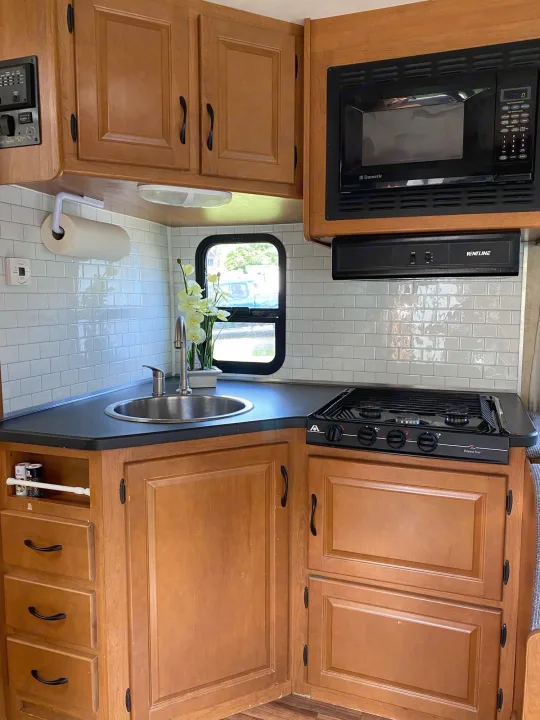 Modern RV rental kitchen with microwave, stove, sink, and subway tile backsplash. Ready for adventure!. Thor Majestic 2013