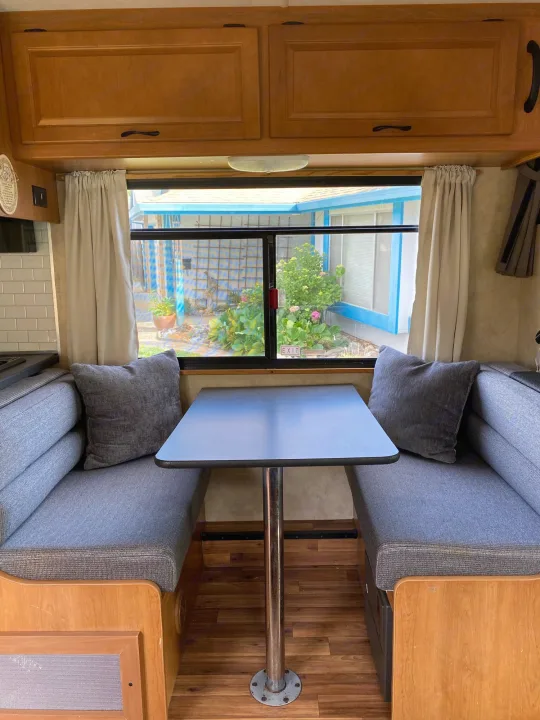 Cozy RV rental dinette with gray upholstered benches, a table, and a large window looking out to a garden setting.. Thor Majestic 2013