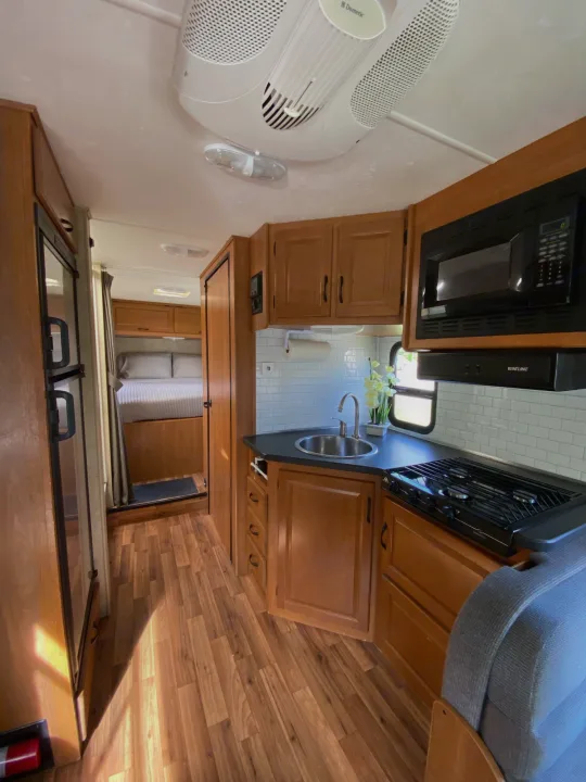 Clean rv rental with a modern kitchen, refrigerator, and a glimpse into the cozy bedroom, featuring wood-look flooring.. Thor Majestic 2013