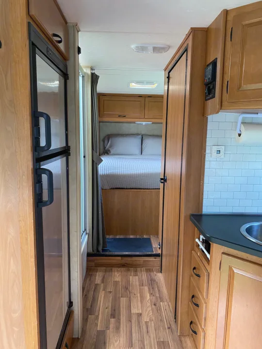Interior of an RV rental: bedroom, kitchen with tile backsplash, refrigerator, and wood floors visible.. Thor Majestic 2013