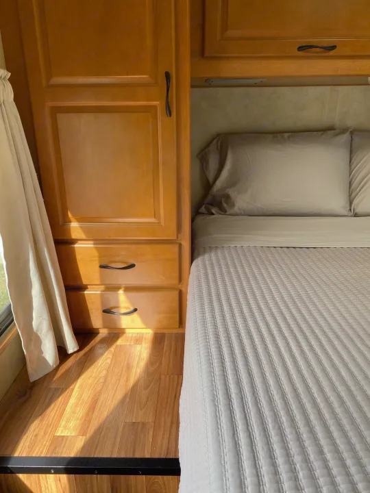 Cozy RV rental bedroom featuring a neatly made bed, wooden cabinets, and sun-drenched wood floor.. Thor Majestic 2013