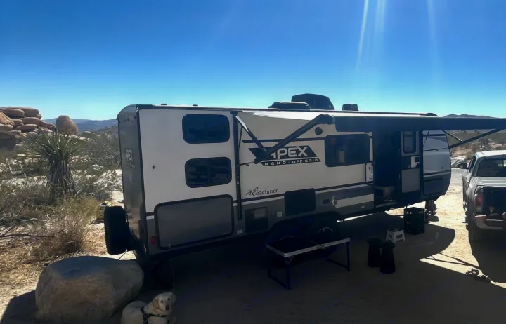 Off-grid rv rental travel trailer, dog, and truck parked in a sunny desert landscape with rocks and yucca plants.. Forest River Coachmen Apex Nano Off-Grid 2022