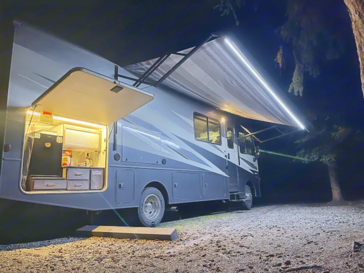 Brightly lit RV rental camping at night, showcasing its open outdoor kitchen and extended awning.. Winnebago Vista 2022