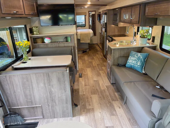 RV rental interior with wood-look flooring. Features a full kitchen, dinette, and comfortable living area with couch.. Winnebago Vista 2022
