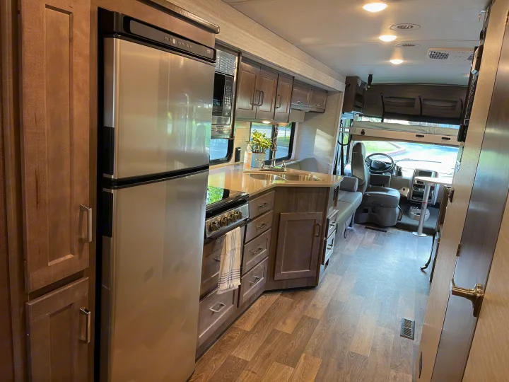 Spacious, modern RV rental interior showcasing a full kitchen with stainless steel appliances, dining area, and driver's cockpit.. Winnebago Vista 2022