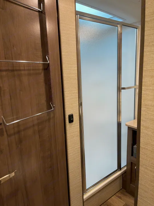 RV rental amenities: a contemporary bathroom with a frosted glass shower, a door featuring towel racks, and a light switch.. Winnebago Vista 2022