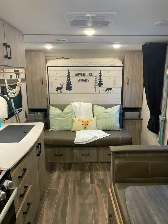 This cozy RV rental interior features a fold-down bed, sofa, and kitchen. Adventure awaits in this modern camping space.. Keystone RV Passport SL 2021