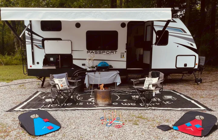 This RV rental showcases a comfortable travel trailer with an extended awning, outdoor kitchen, fire pit, chairs, and games.. Keystone RV Passport SL 2021