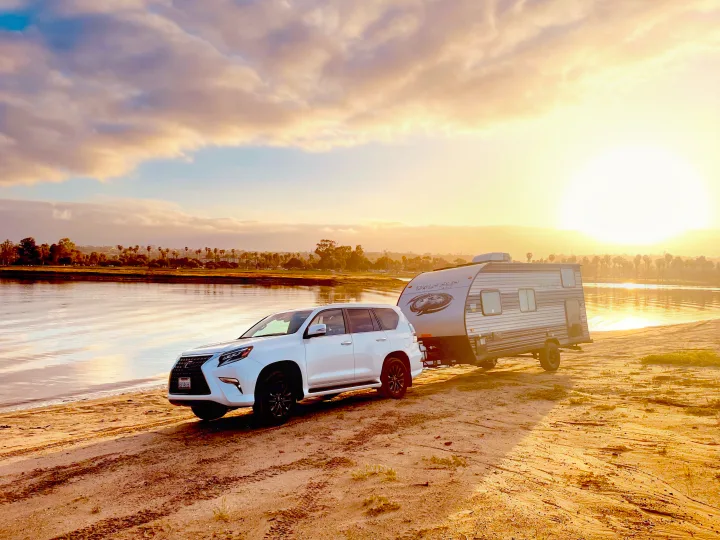 White Lexus GX SUV with a Wolf Pup RV rental trailer parked on a sandy shore by water during golden hour. Ready for adventure.. Forest River Cherokee Wolf Pup 2022