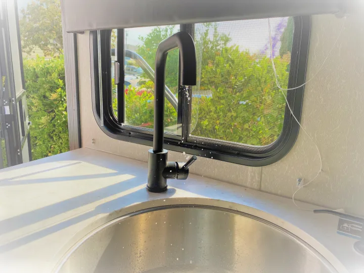 Bright RV rental kitchen: black faucet, stainless sink, sunny window with greenery. Water droplets visible on surfaces.. Forest River Cherokee Wolf Pup 2022