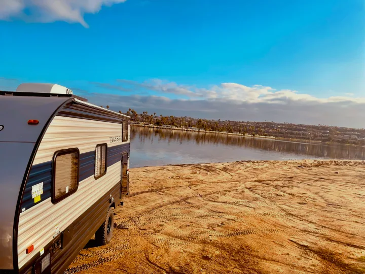 This RV rental enjoys a scenic spot, a travel trailer parked on sand next to a calm bay with a distant city under a blue sky.. Forest River Cherokee Wolf Pup 2022